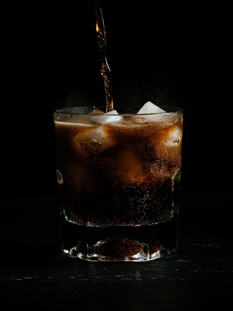 Vertical shot of coke being poured in a glass full of ice on a black background